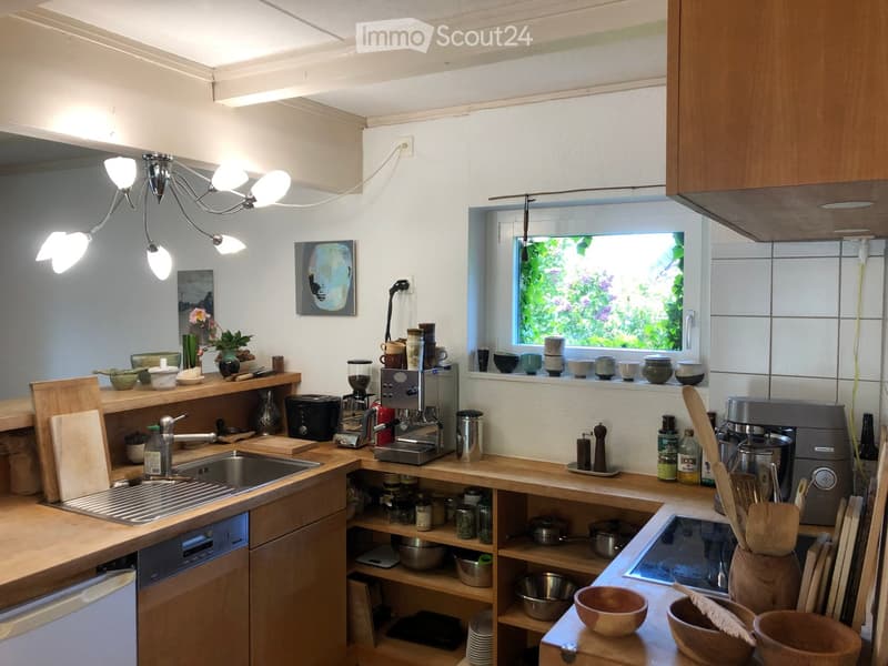 Bright, modern kitchen with wooden countertops, stainless steel appliances, and ample natural light from a window. Features include a sink, coffee maker, toaster, cutting board, and various kitchen utensils and decor.