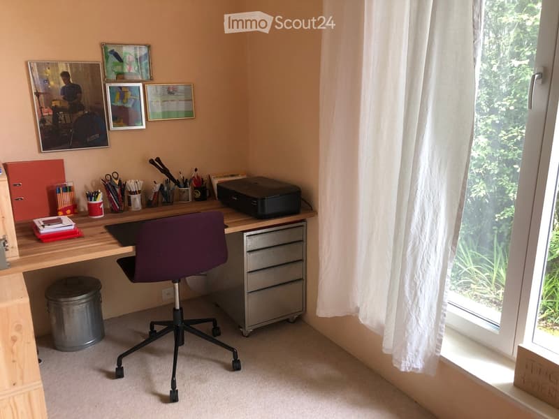 A well-organized home office with a wooden desk, purple office chair, printer, and various office supplies. The room features framed artwork on the walls and a large window with white curtains.