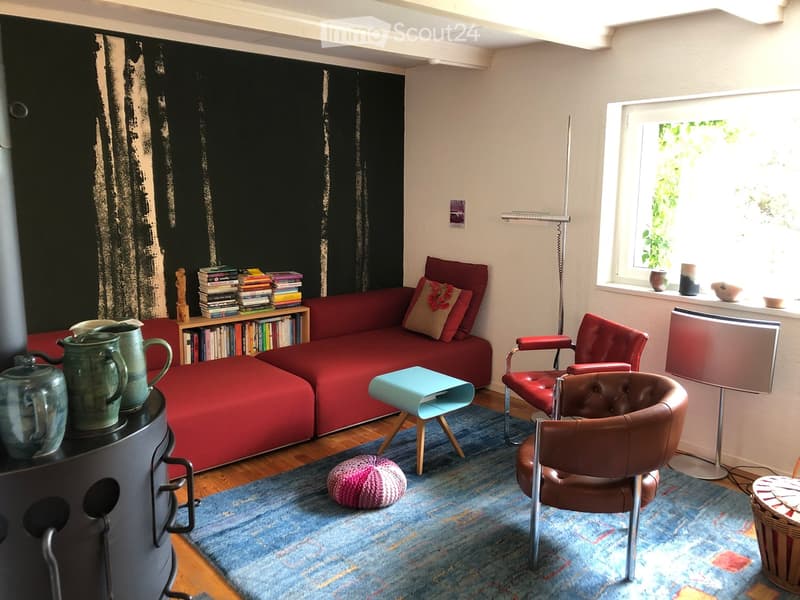 Modern living room with a red sectional sofa, two red armchairs, a blue side table, a bookshelf, a fireplace, and a colorful rug.