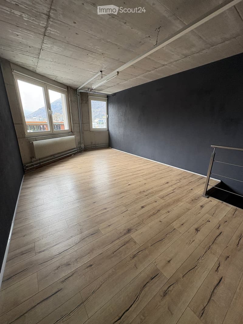 Empty room with wooden flooring, dark grey walls, and large windows offering a view of the mountains.