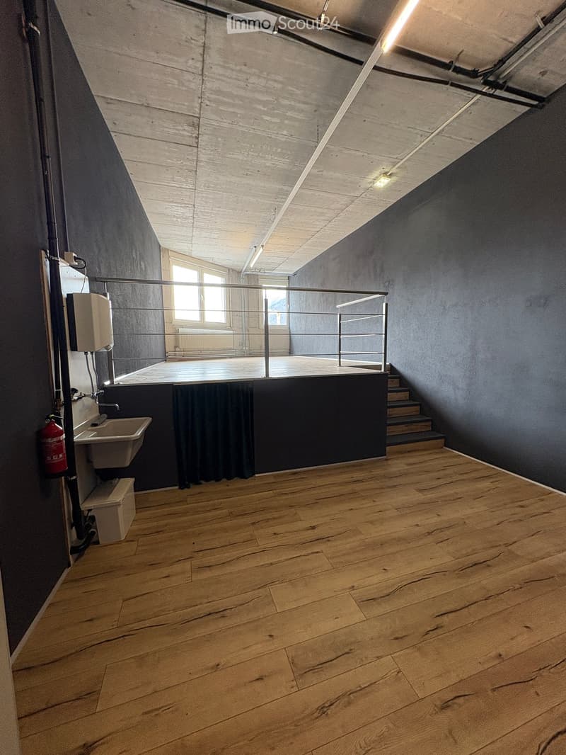 Empty room with wooden flooring, dark walls, a staircase leading up, a small sink, and a window with a metal railing.