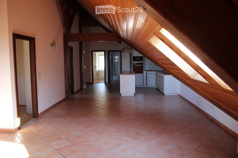 Bright hallway with wooden beams and exposed ceiling, leading to a kitchen area with white cabinets and appliances.