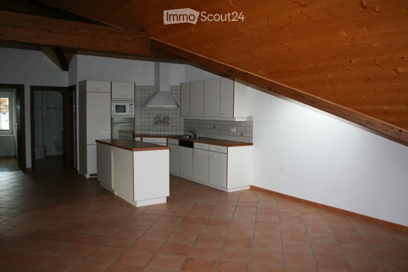Bright kitchen with white cabinets, a refrigerator, microwave, and a sink. The space features a wooden slanted ceiling and terracotta tiled flooring.