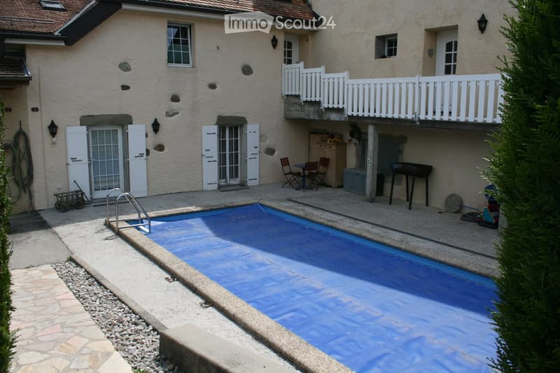 Outdoor area with a swimming pool, patio furniture, barbecue, and a balcony overlooking the area.