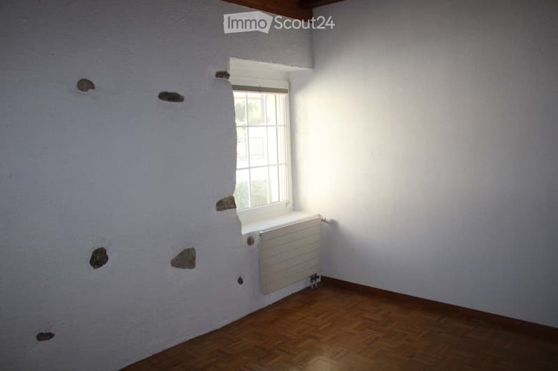 Empty room with wooden flooring, white walls, and a single window with a radiator below it. The walls have visible patches and holes.