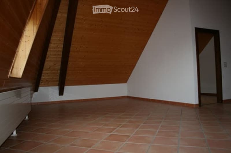 Empty attic room with wooden slanted ceiling, tiled floor, and a doorway leading to another space.