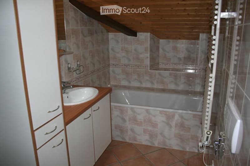 Bathroom with a sink, bathtub, and white cabinets. The walls are tiled with a floral pattern, and the floor is tiled in a warm terracotta color.