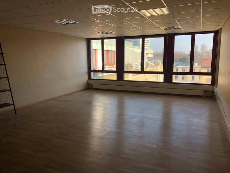 Empty room with wooden flooring, large windows, and a metal shelving unit in the corner.