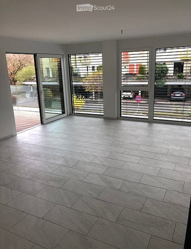 Empty room with large windows, tiled floor, and sliding glass doors leading to a balcony.
