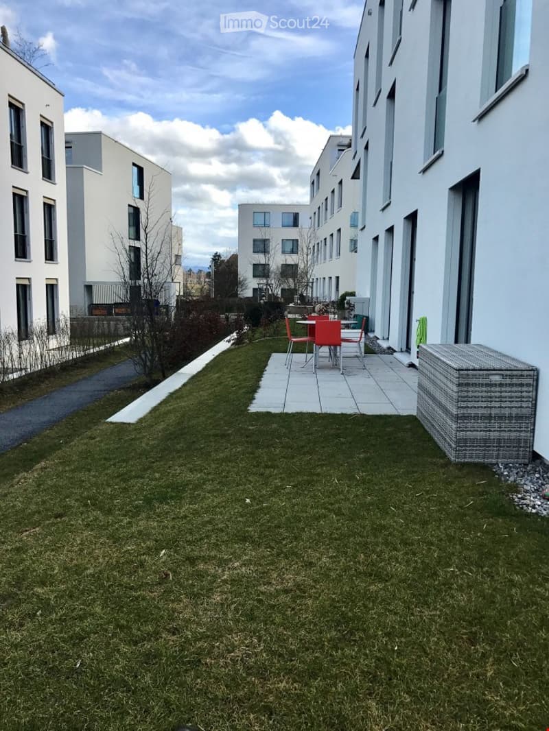 A small garden with a table and chairs, a storage box, and a paved area.