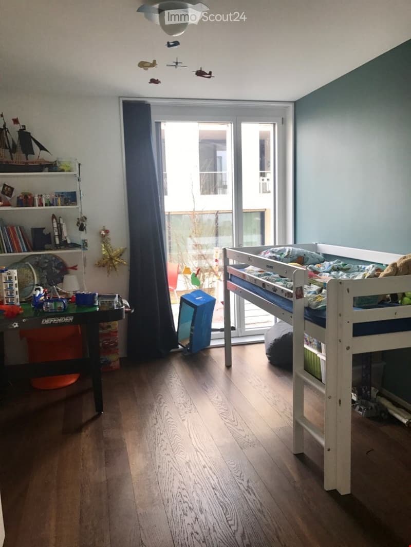 A child's bedroom with a bunk bed, a desk, a shelf with toys, and a glass door leading to a balcony.