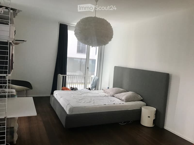 double bed, gray headboard, white bedspread, white pillows, white lamp, white trash bin, white desk, white chair, black curtains, balcony