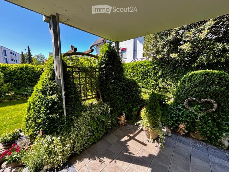 Well-maintained garden with neatly trimmed hedges, a small decorative statue, and a tiled patio area.
