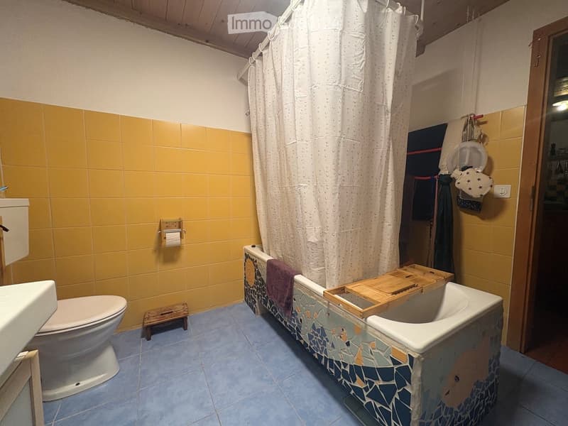 Bathroom with yellow tiled walls, blue tiled floor, white bathtub with mosaic border, toilet, shower curtain, and towels.