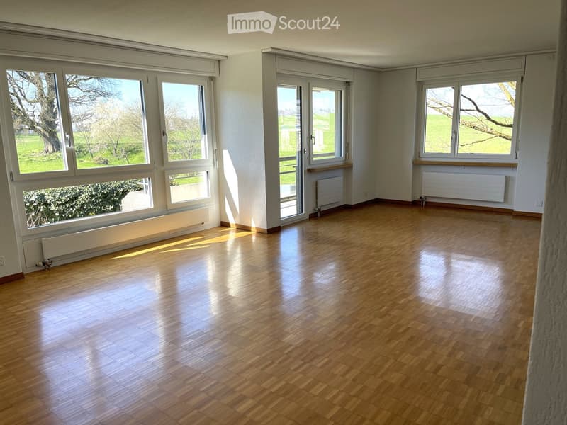 Empty room with wooden flooring, large windows, and radiators along the walls.