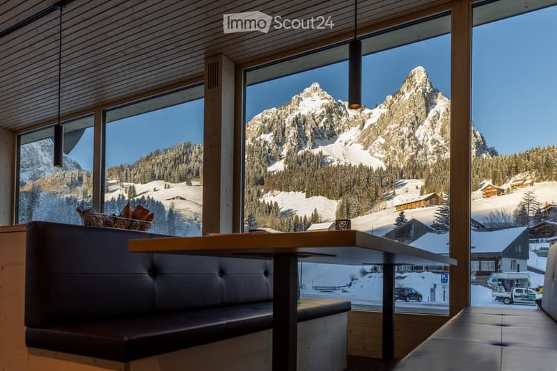 A modern dining area with a wooden table and leather bench, large windows offering a scenic mountain view.