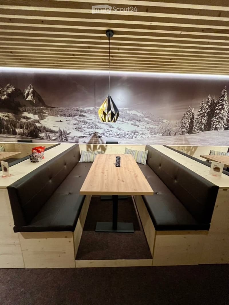 Modern dining area with wooden table, bench seating, and pendant light. Features a scenic mountain mural on the wall.