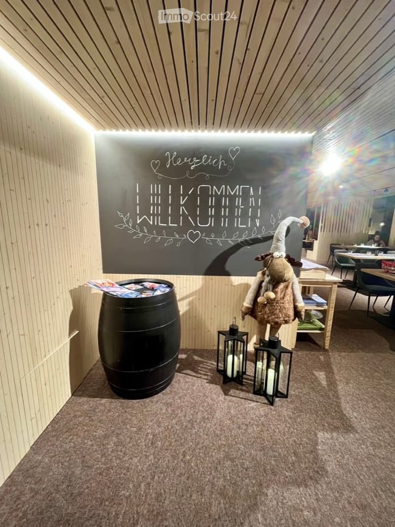 A cozy, modern reception area with a wooden barrel, a plush toy on a stool, lanterns, and a welcoming sign on the wall.