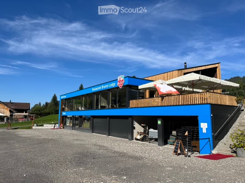 Modern two-story building with blue facade, large windows, and outdoor seating area with umbrellas.