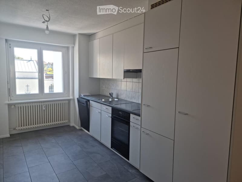 Modern kitchen with white cabinets, stainless steel sink, oven, dishwasher, and tiled floor.