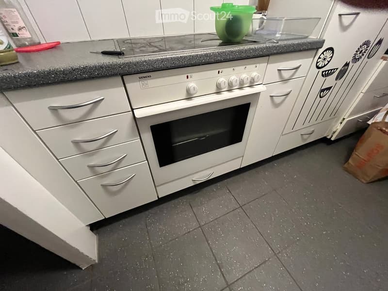 A kitchen with white cabinets, a Siemens oven, a grey countertop, and various kitchen items on the counter.