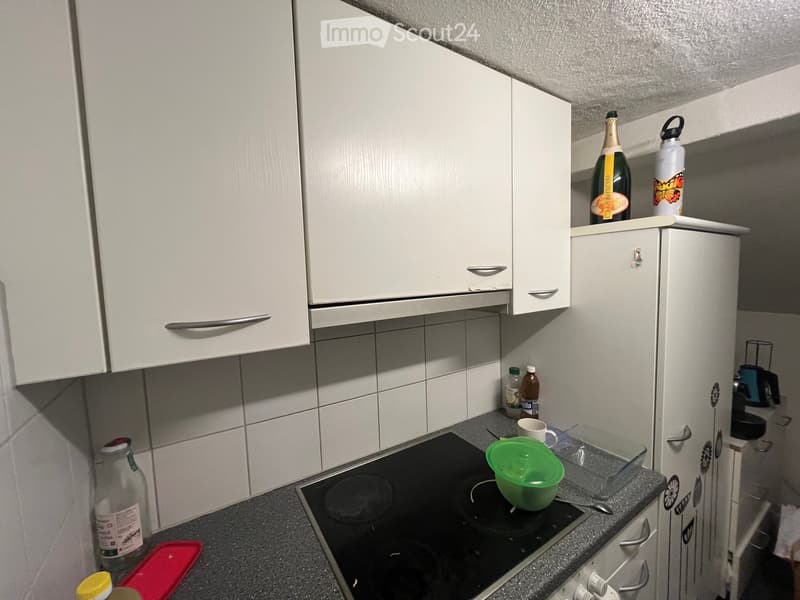 Modern kitchen with white cabinets, an induction stove, and various items on the counter including a green bowl, a cup, and several bottles.