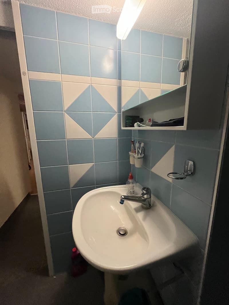 A small bathroom with a white sink, a mirror cabinet, and a toothbrush holder. The walls are tiled in blue and white with geometric patterns.