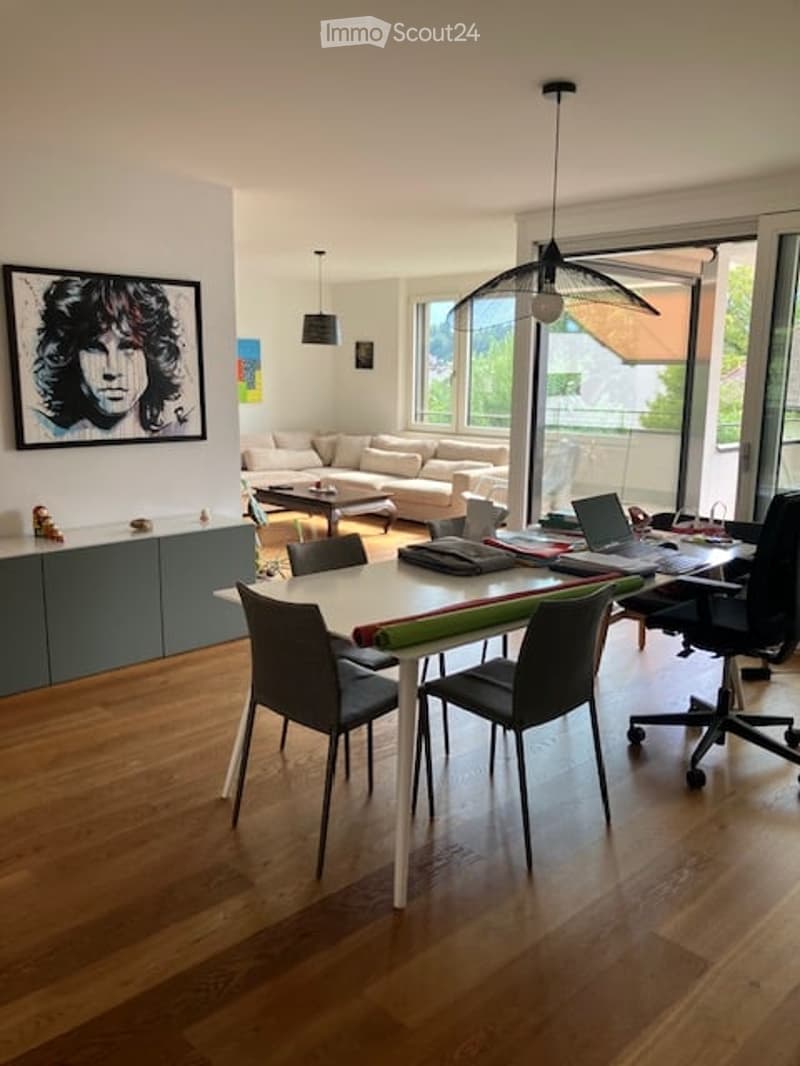 Open-plan living and dining area with modern furniture, large windows, and a balcony view.
