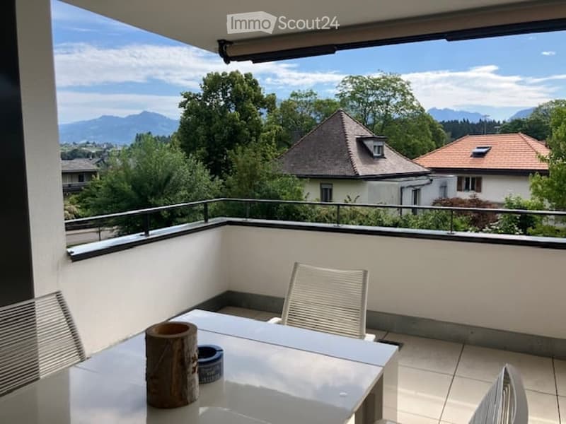 Balcony with a view of mountains and houses, featuring a table and chairs.