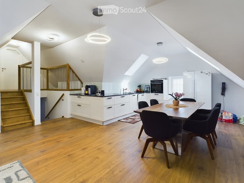 Open-plan kitchen and dining area with wooden floor, white cabinets, modern lighting, dining table, and a staircase leading to the upper floor.