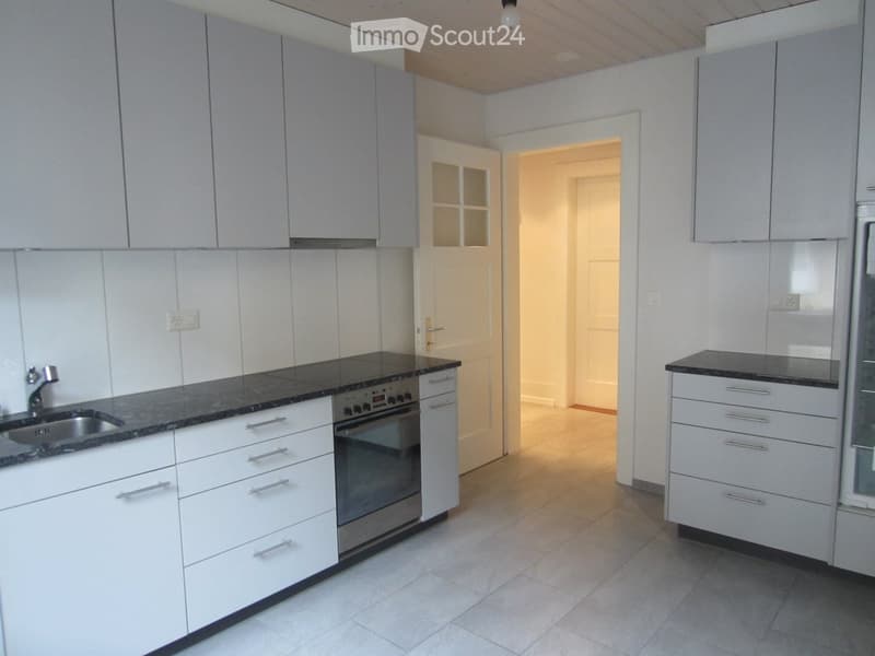 Modern kitchen with white cabinets, black granite countertops, stainless steel sink and oven, and a doorway leading to another room.