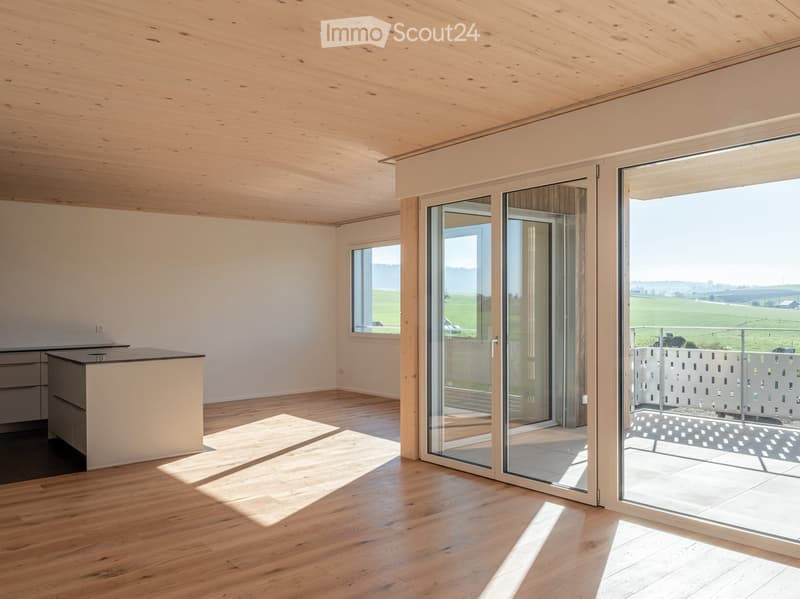 Bright, modern kitchen with wooden floors, white walls, and large glass doors opening to a scenic outdoor view.