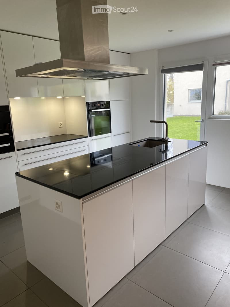 Modern kitchen with white cabinets, black countertop, stainless steel sink, faucet, oven, and range hood. Large window provides natural light.