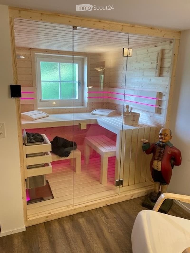 Modern bathroom with a large glass-enclosed shower area, wooden benches, a bathtub, and a decorative statue. Pink LED lighting accents the walls.