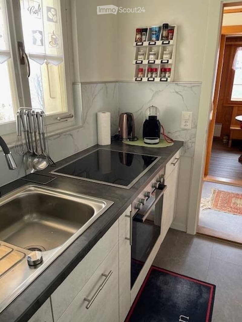 Modern kitchen with white cabinets, black countertops, stainless steel sink, induction cooktop, oven, coffee maker, and spice rack.