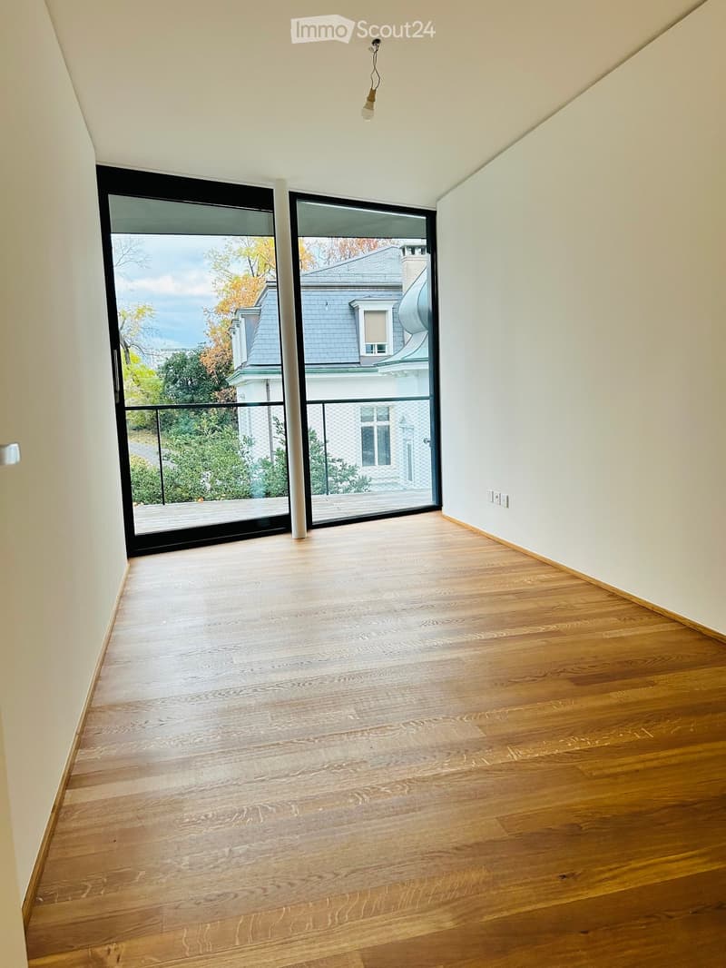 Empty room with wooden flooring, white walls, and large sliding glass doors leading to a balcony with a view of the outside area.