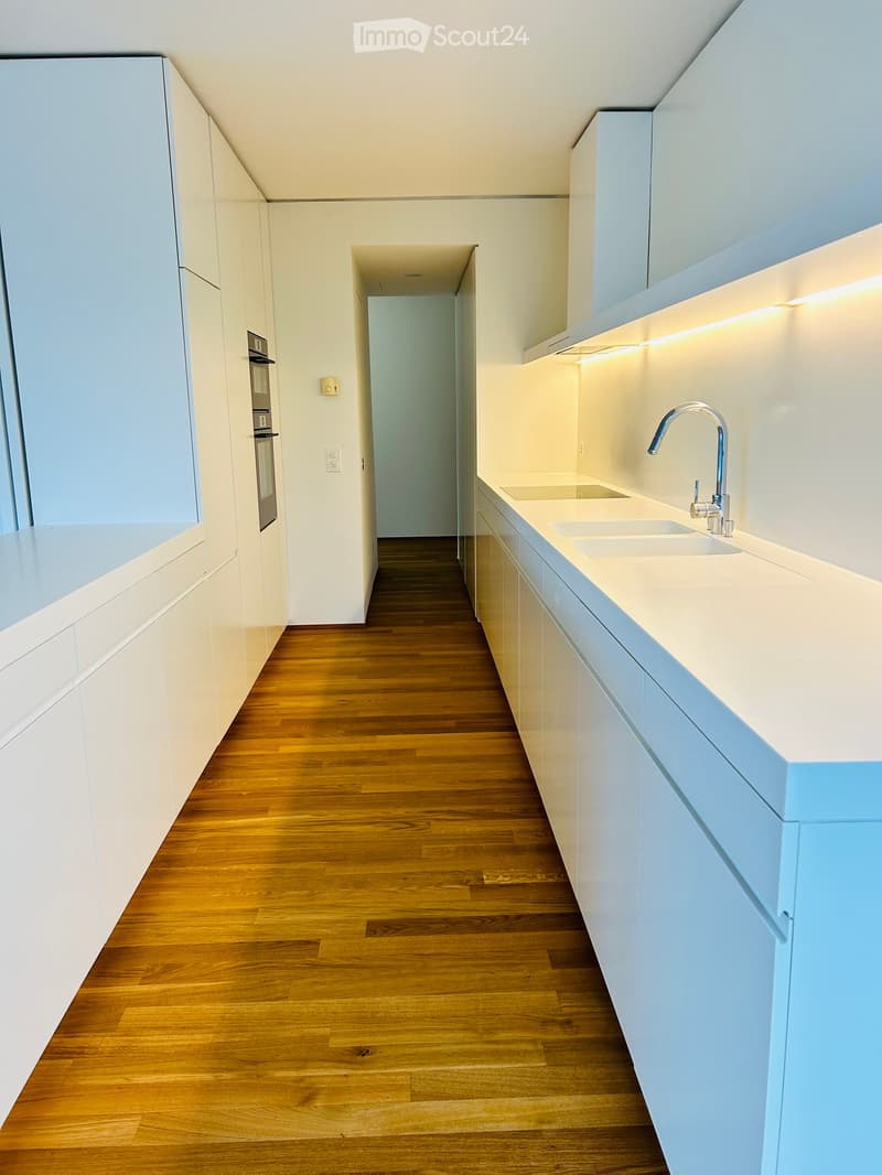 Modern kitchen with light blue cabinets, white countertops, and a double sink with a modern faucet. The floor is made of polished wood.