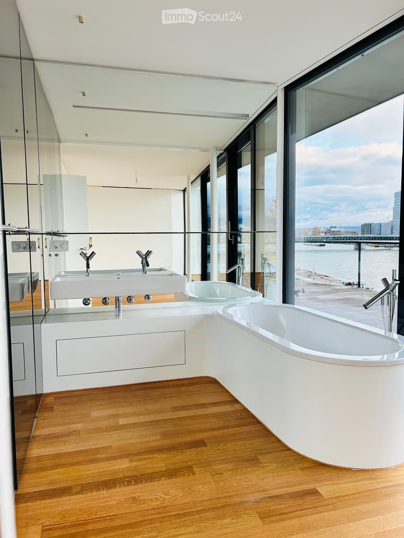 Modern bathroom with a freestanding bathtub, double sink, and large windows offering a view of the water.