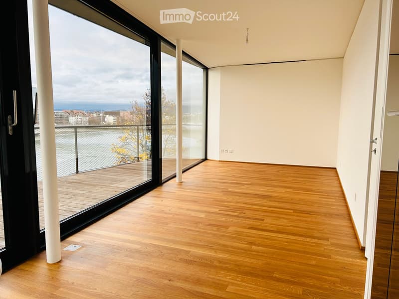 Empty room with wooden flooring, large glass sliding doors leading to a balcony, white walls, and a view of the city.