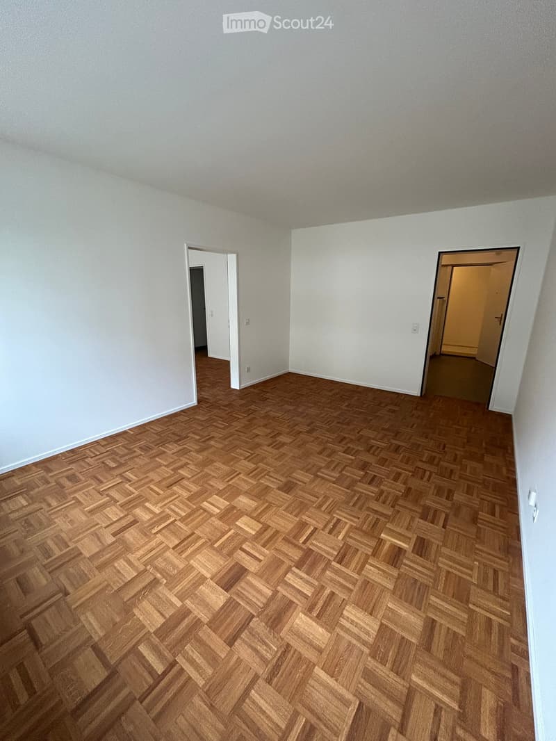 Empty room with wooden herringbone flooring and white walls, featuring two open doorways leading to adjacent spaces.