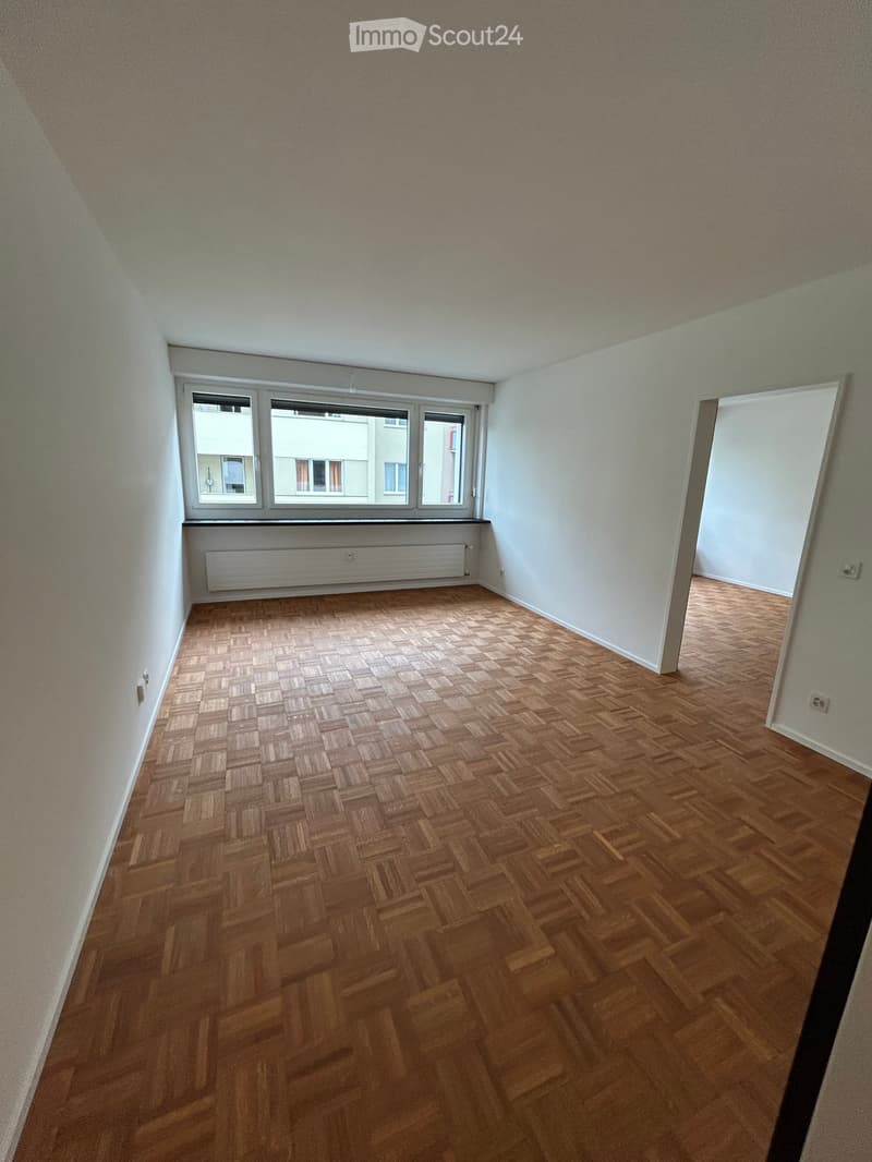 Empty room with wooden herringbone flooring, white walls, and large windows with a radiator below. No furniture or equipment present.