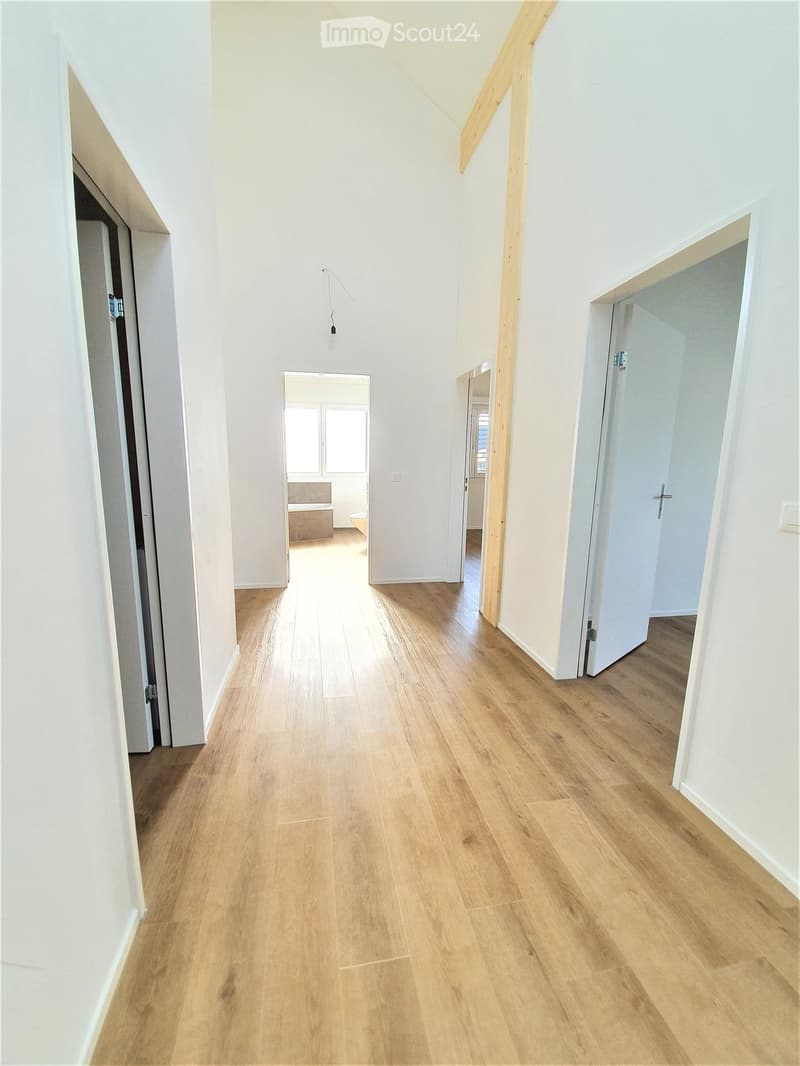 Empty hallway with light wooden flooring, white walls, and several doors leading to other rooms.