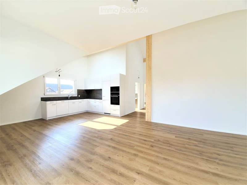 Bright, open room with wooden flooring, white cabinets, a sink, microwave, and oven. The space is clean and well-lit with large windows.