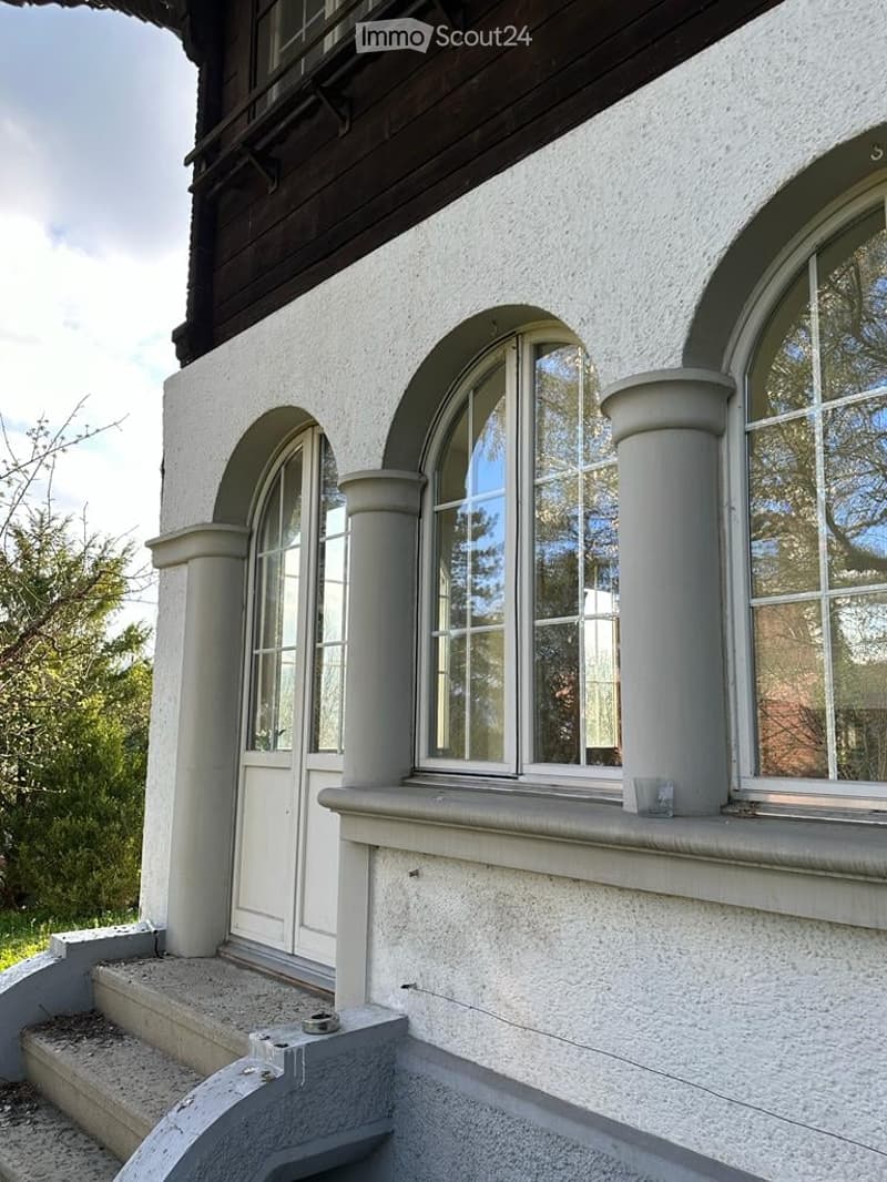 white exterior, arched windows, wooden door, concrete steps, concrete pillars