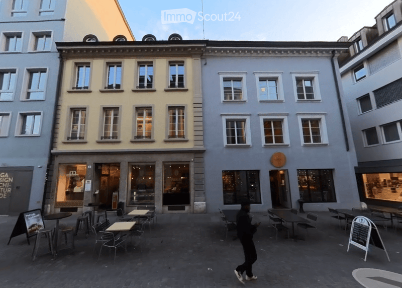 Two-story building with multiple windows and a ground-floor restaurant area featuring outdoor seating with tables and chairs.