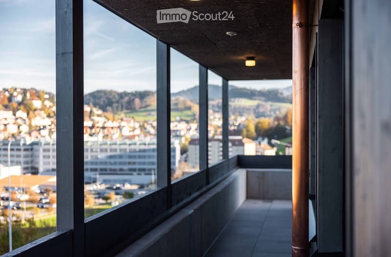 A balcony with a view of the city and mountains, featuring a tiled floor and a copper pipe.