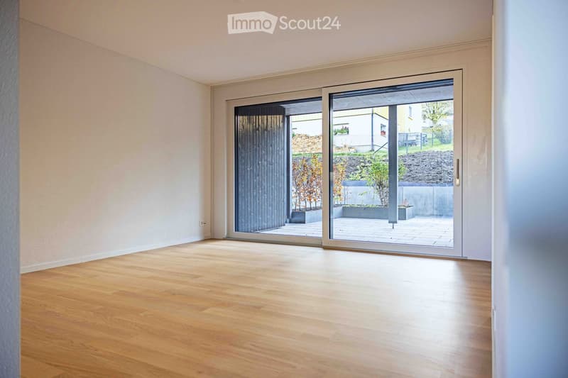 Empty room with white walls, wooden floor, and sliding glass doors leading to a patio.