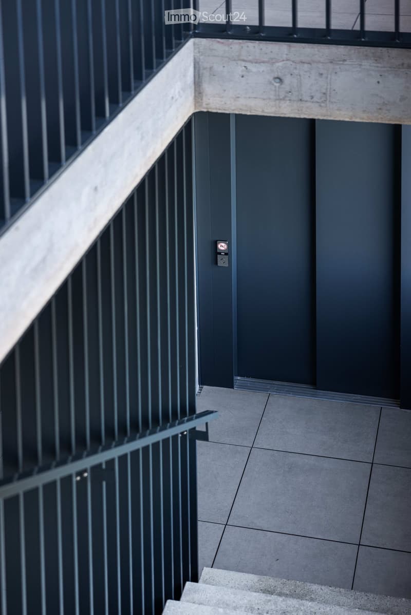 A modern corridor with a concrete floor, metal railings, and an elevator door.