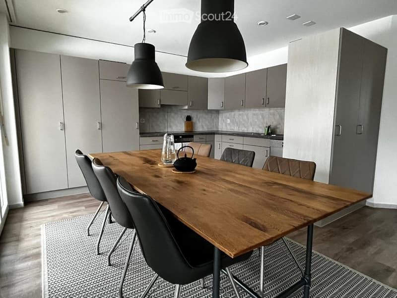 Modern dining area with a wooden dining table, black chairs, grey cabinets, and pendant lights.