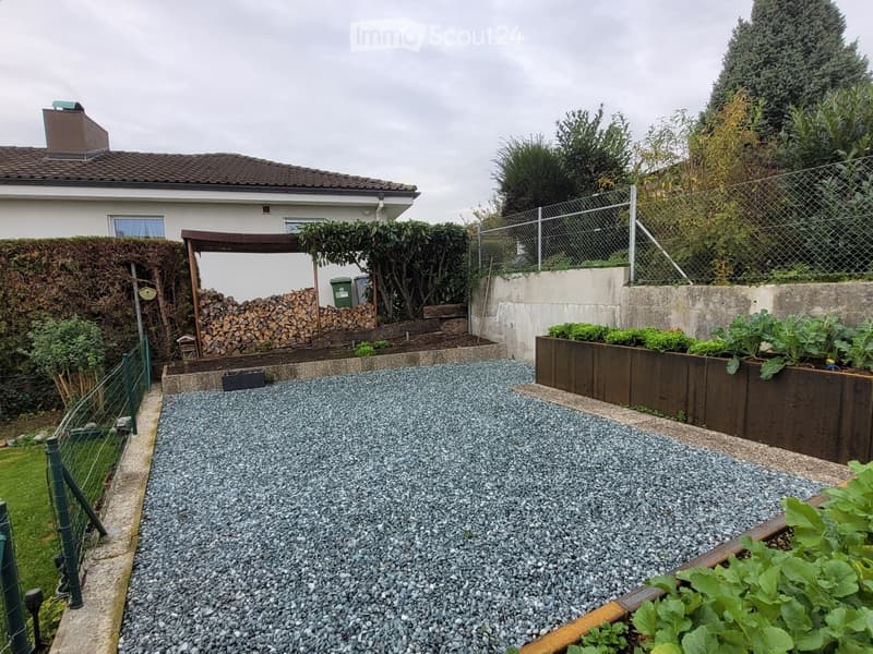 Backyard with gravel-covered ground, raised garden beds, wooden fence, and a stack of firewood.